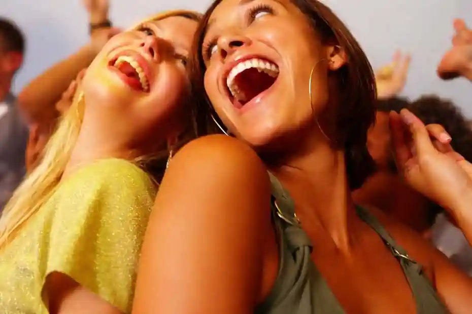Duas mulheres sorrindo amplamente em contexto social, imagem usada para análise de congruência emocional e identificação de sorriso falso.