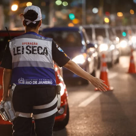 Agente da Operação Lei Seca durante blitz noturna, direcionando veículos em fiscalização de trânsito no Brasil.