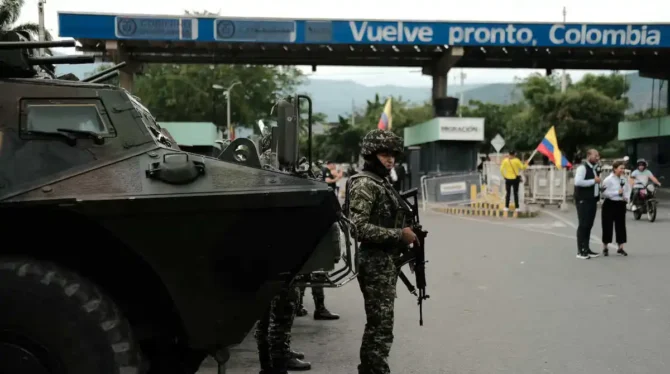 Militar armado em posto de fronteira na Colômbia, com veículo blindado e faixa “Vuelve pronto, Colombia”, em imagem sobre segurança pública e endurecimento penal.